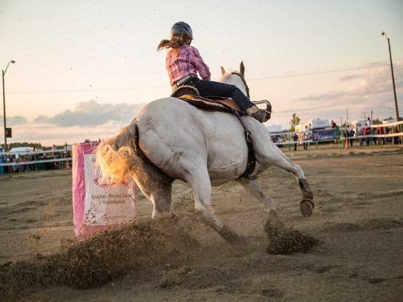 La photo présente une cavalière sur son cheval pendant une course de barils lors du Festival western et rodéo professionnel de La Sarre.