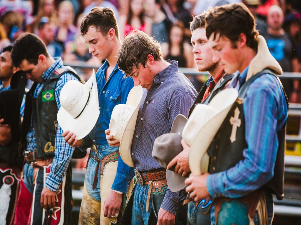 La photo présente des cowboys en position solonelle pendant la prière d'ouverture lors du Festival western de Guigues. 