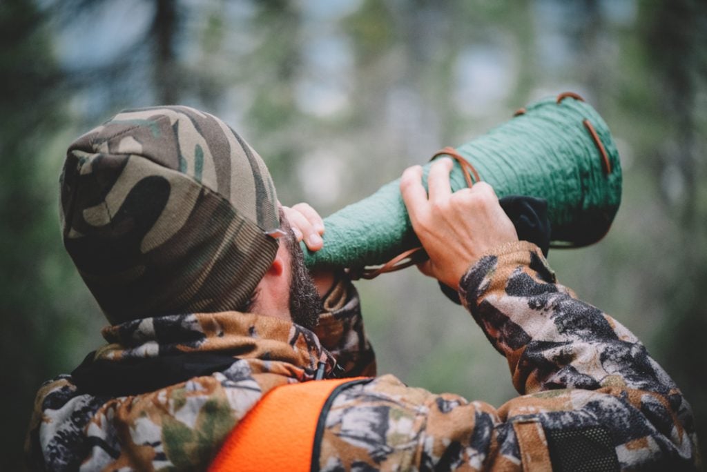 Un homme à la chasse, callant l'orignal en habit de camouflage et dossard orange dans la forêt