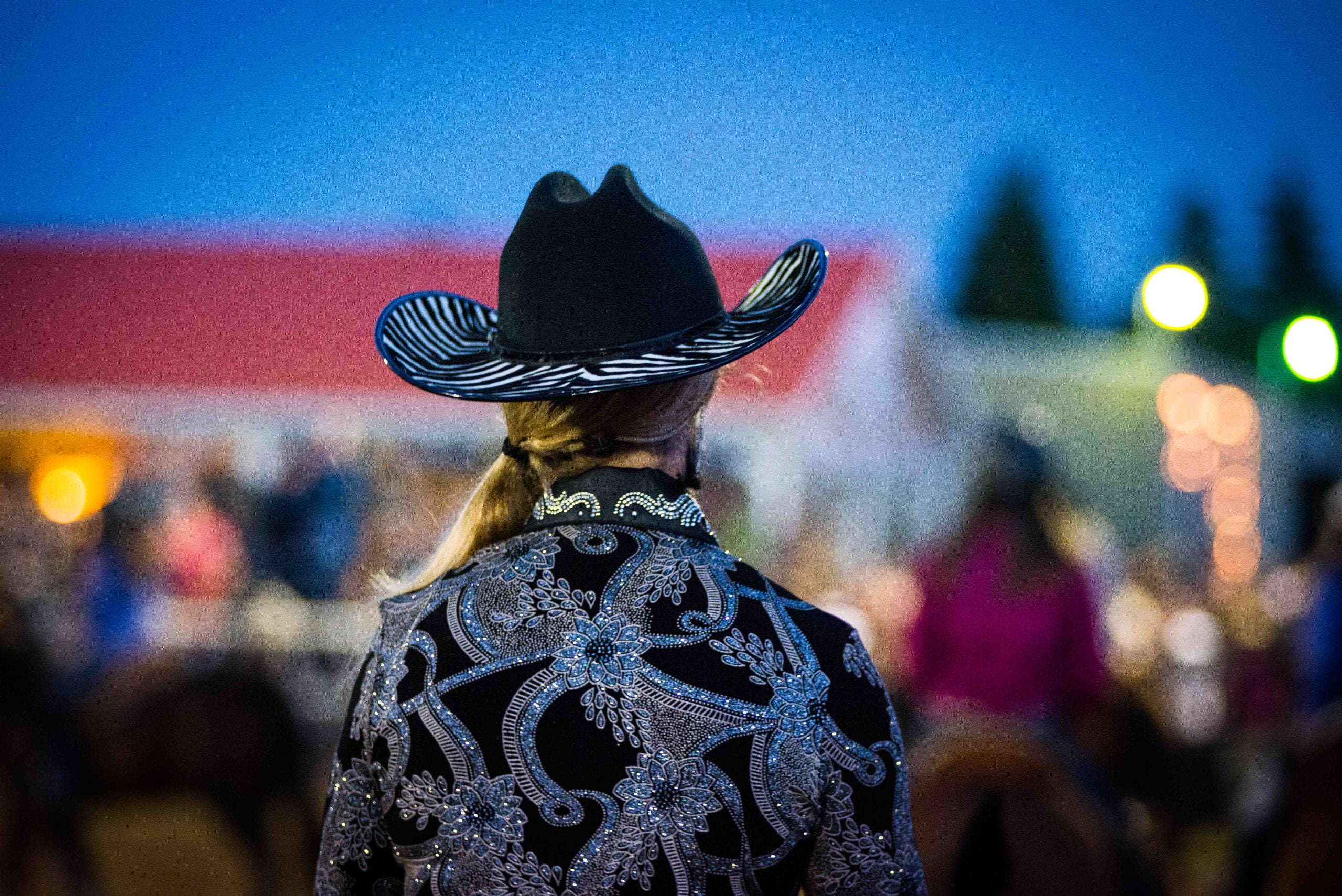 La photo présente une cowgirl de dos dans un bel habit noir serti de paillettes argentées lors du Festival western de Guigues.