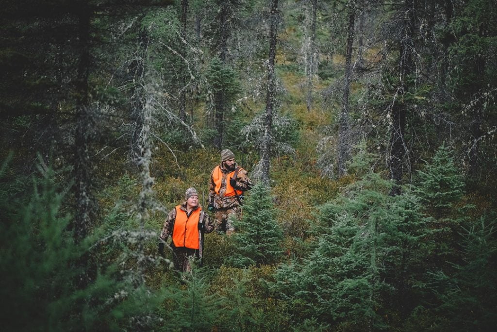 Un homme et une femme à la chasse en habit de camouflage et dossard orange dans la forêt