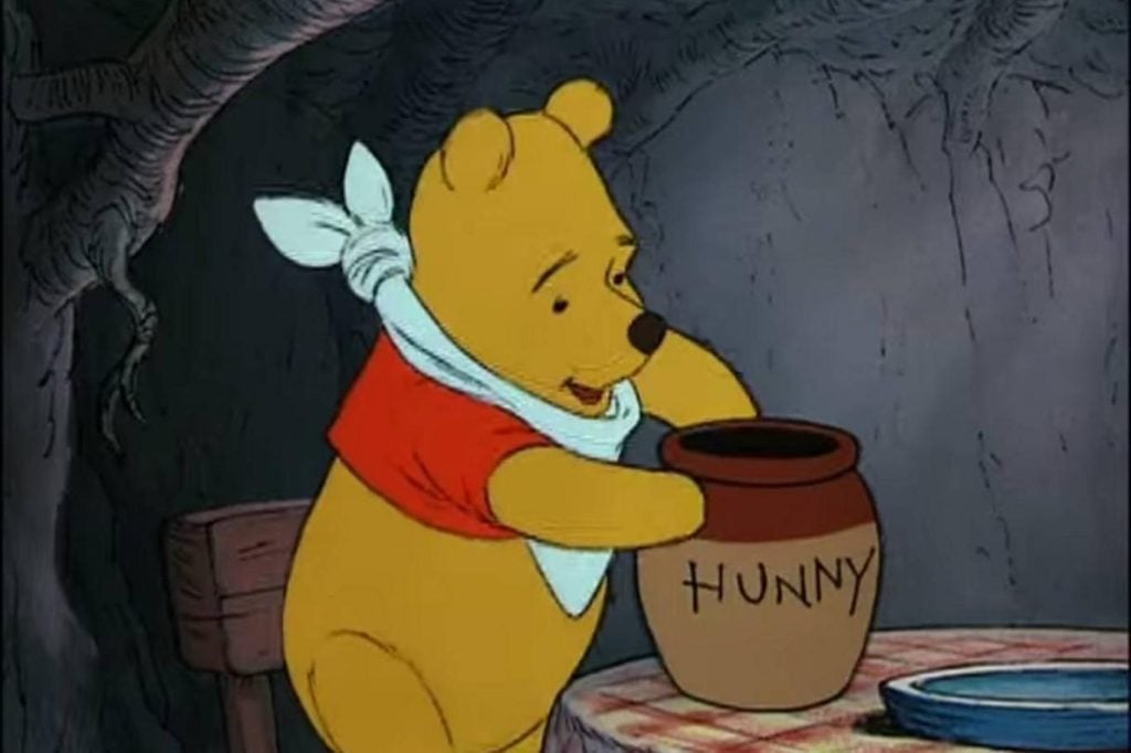 Winnie l'ourson porte un bout de tissus en guise de bavette afin de protéger son unique chandail rouge. Il tient un pot brun sur lequel se trouve le mot "miel".