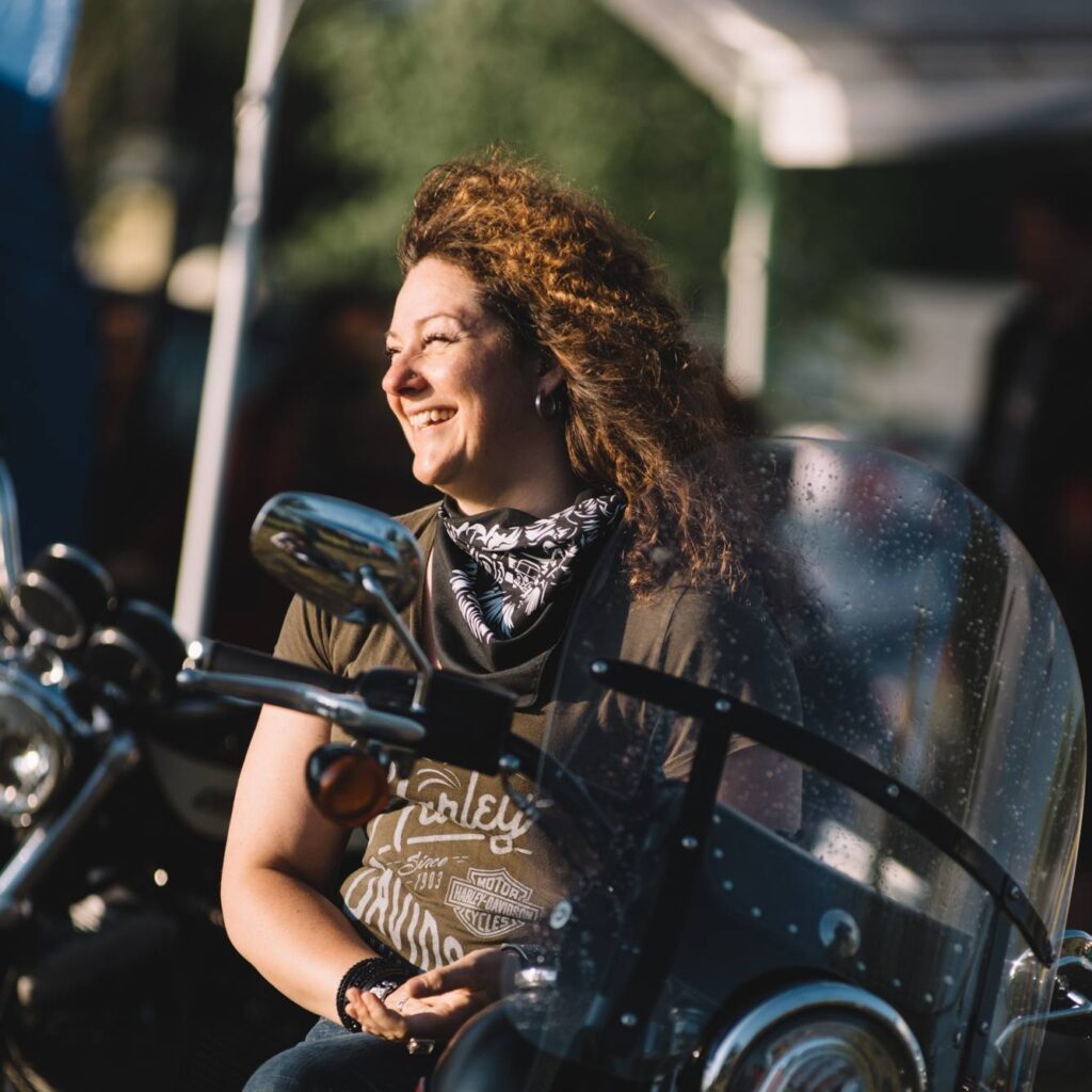 Une femme motocycliste est assise sur sa moto et elle sourit à pleines dents.